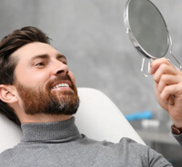 Happy cosmetic dental patient looking in hand mirror