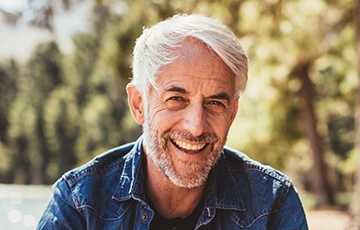 Older man in denim shirt smiling outdoors
